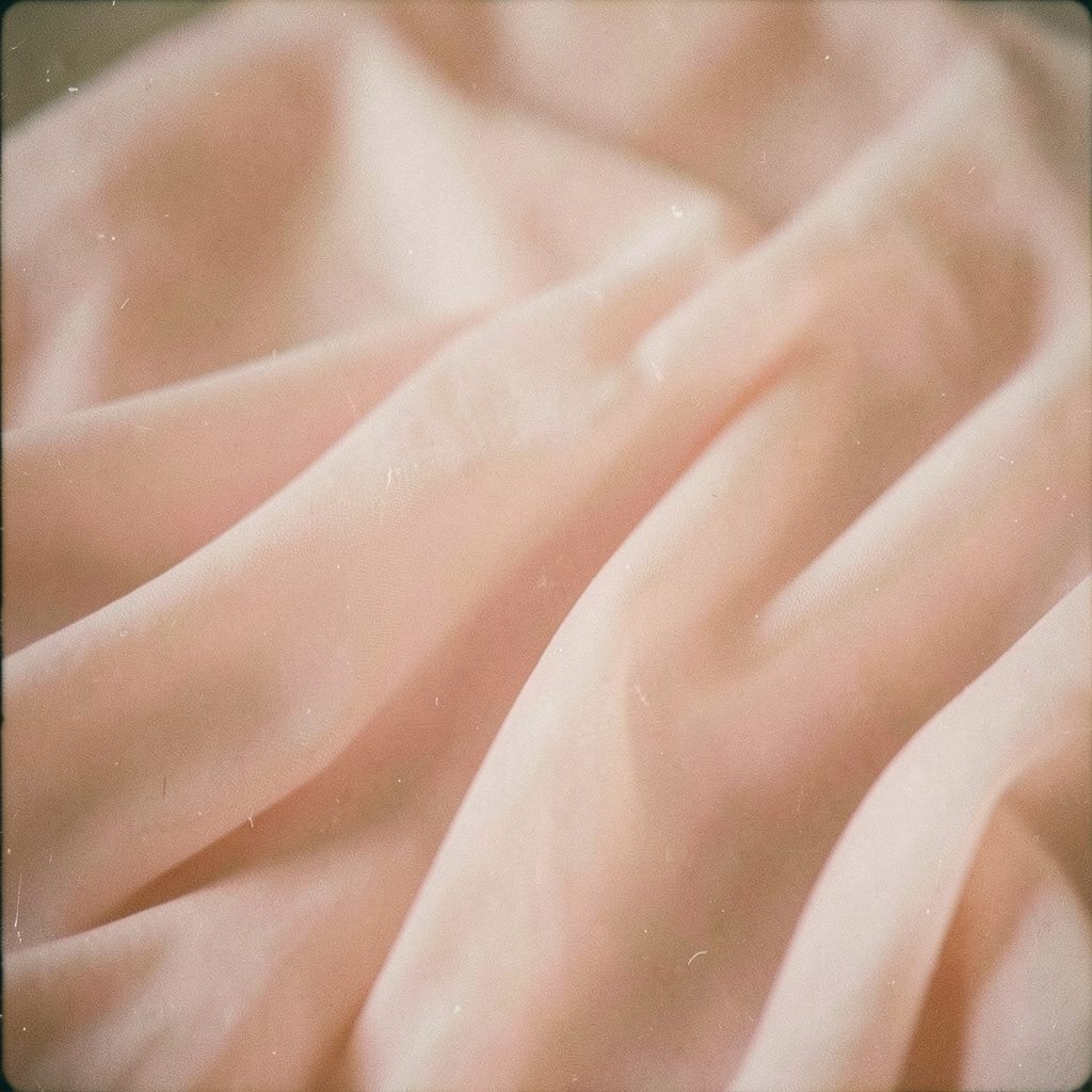 Analog photograph of delicate fabric in blush pink tones, gently draped, visible film grain, warm and feminine mood.